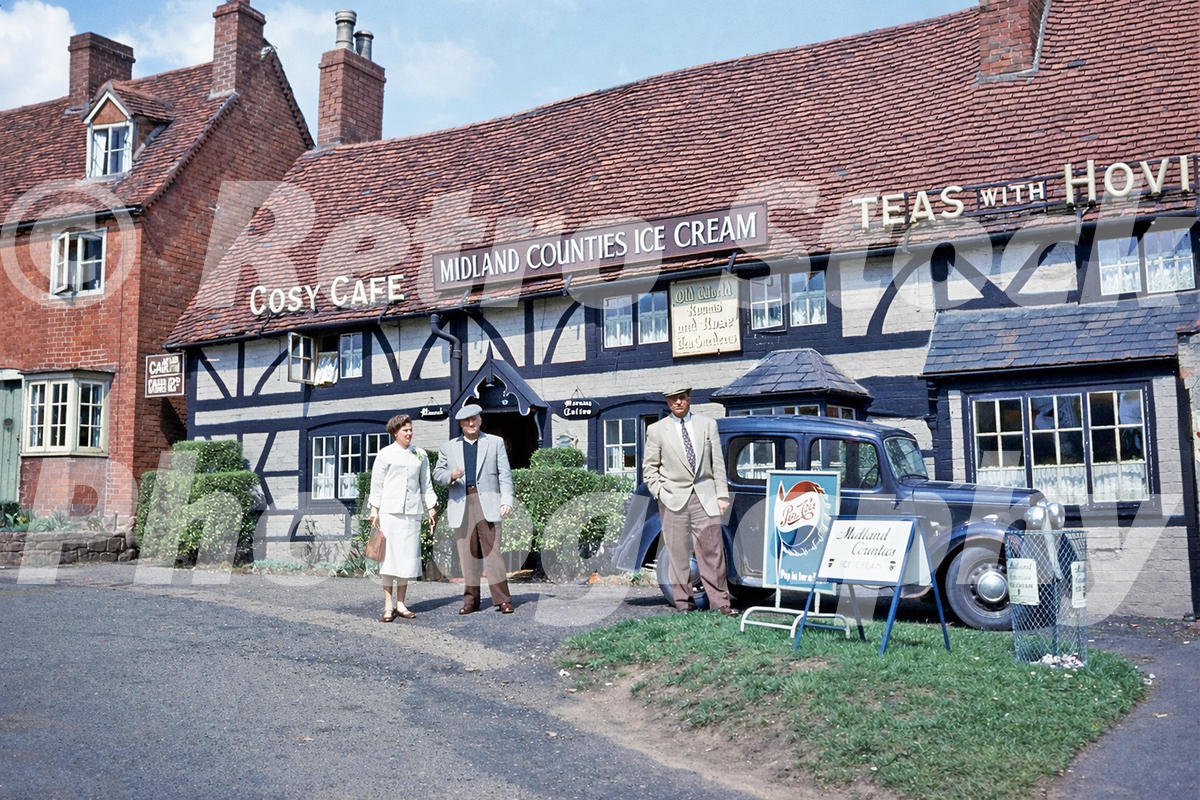 1950s view of the Cosy Cafe on Castle Green in Kenilworth, with cafe signs, people outside and a parked Austin car.