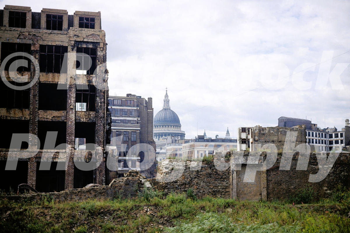 A 1950s colour photo of the skeletal remains of a bomb-damaged building in Cripplegate, London, with the distant dome of St. Paul’s Cathedral visible through the ruins.