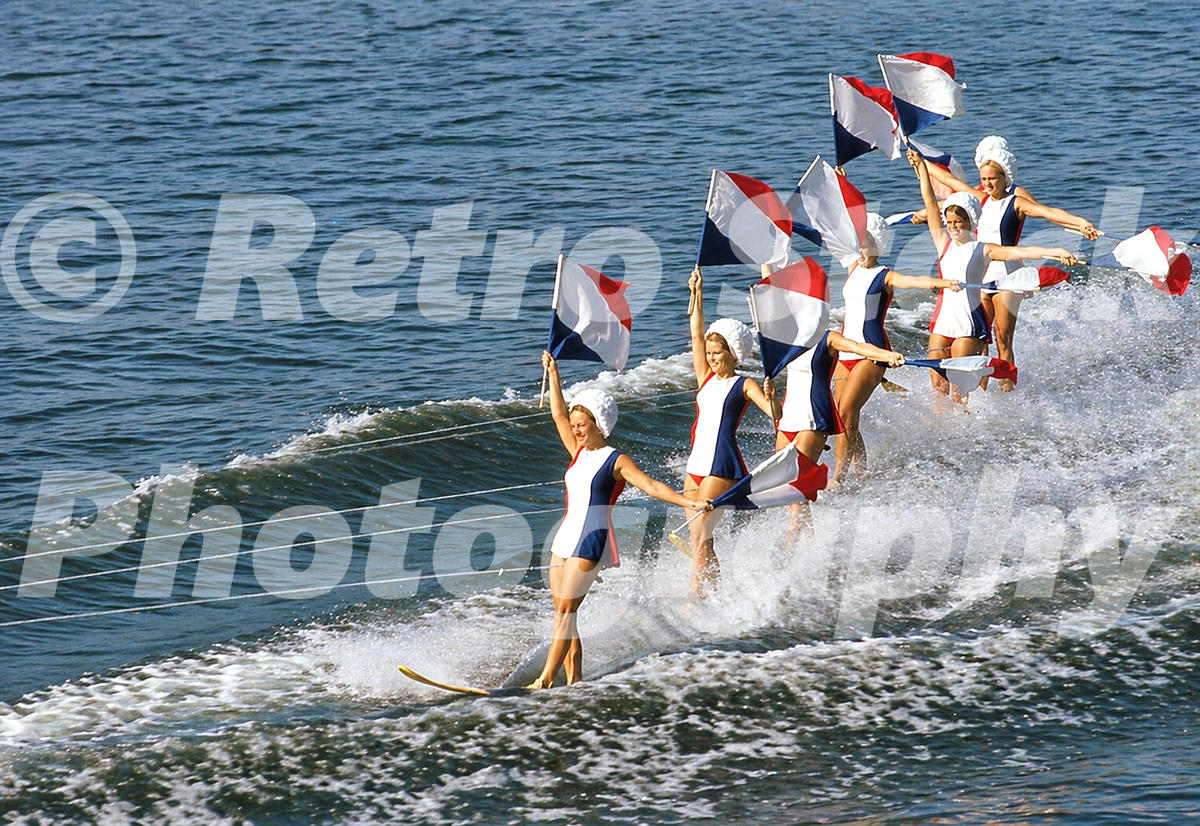 1960s color view of women water skiers performing with red, white and blue flags at Cypress Gardens in Winter Haven, Florida.
