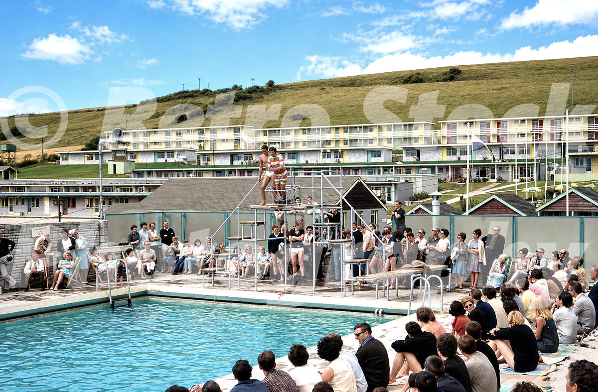 Pontins Osmington Bay outdoor pool in the 1960s with diving platform performers, spectators and hillside accommodation blocks