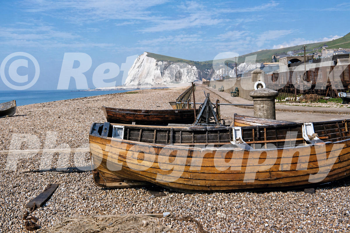 1950s view of Dover Beach with wooden boats on the shingle and white chalk cliffs in the background.