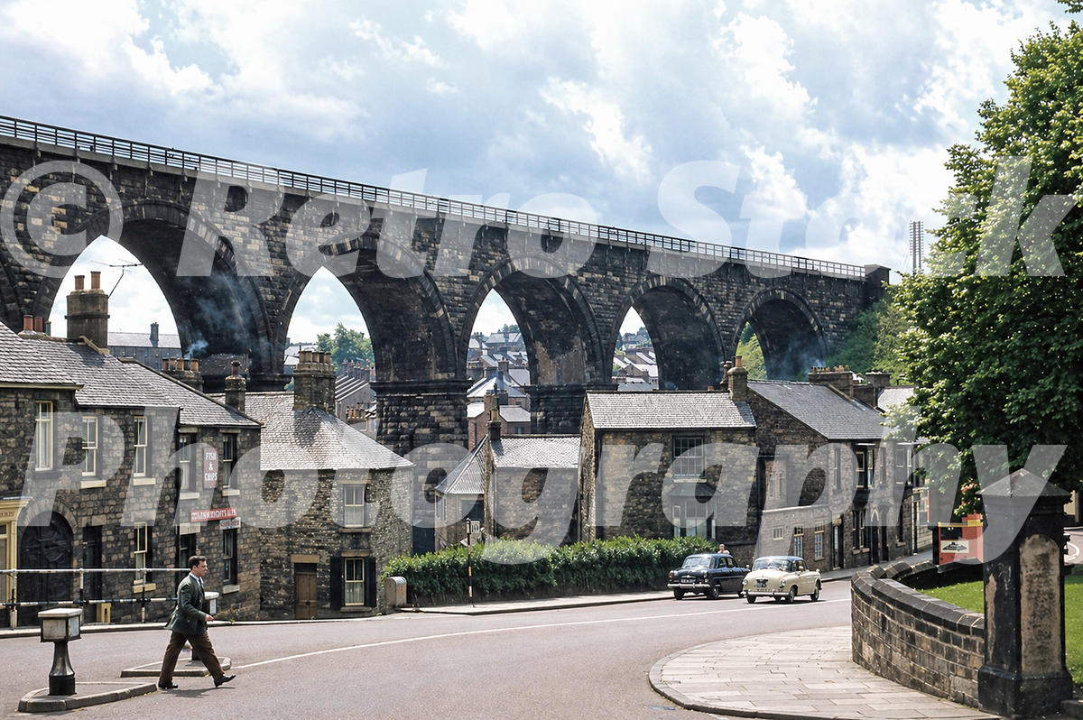 1950s view of Durham Viaduct in County Durham rising above stone houses, a curved road and period cars below
