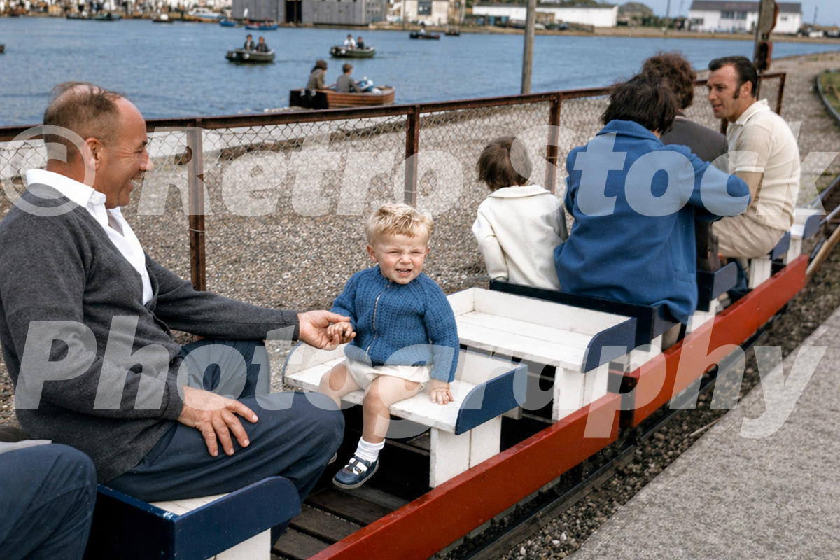 1960s view of passengers on Hastings Miniature Railway, with the boating lake and rowing boats n the background.