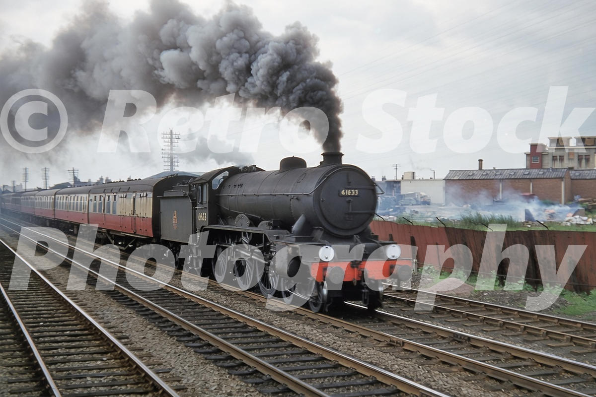 1950s view of LNER B17 No. 61633 Kimbolton Castle at Cambridge hauling a passenger train past sidings and industrial buildings with smoke streaming overhead