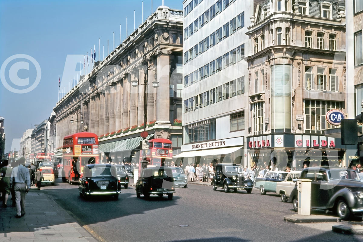 A 1960s colour photo of red double-decker buses and black taxis driving past Selfridges and the Gilda shop on Oxford Street in 1961.