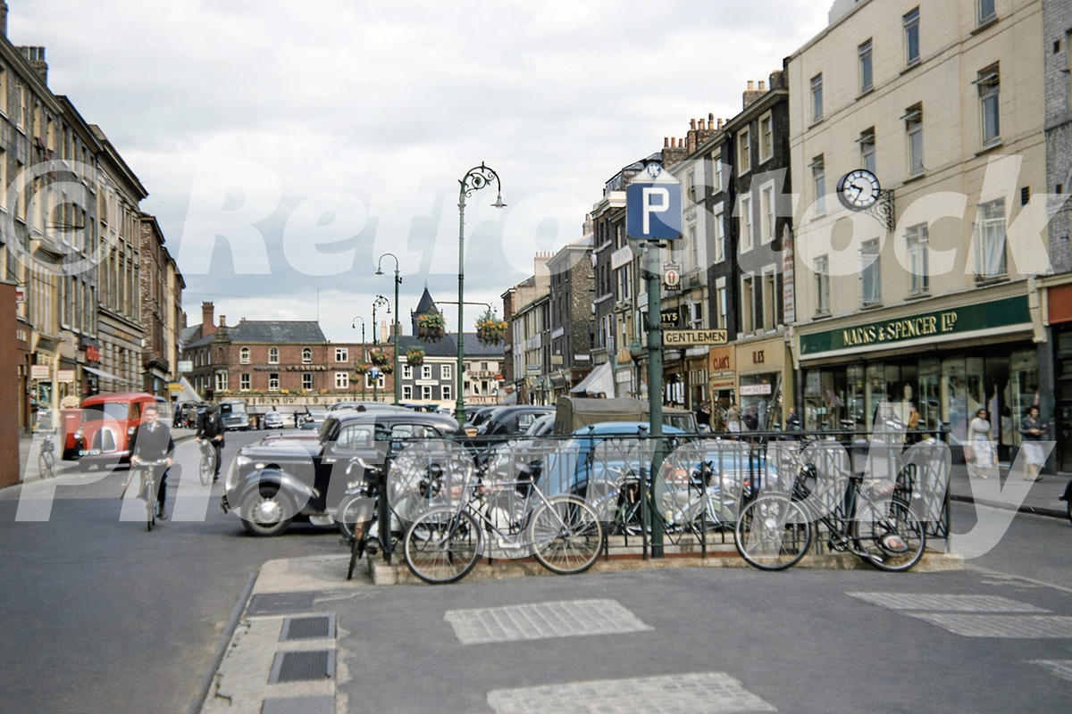 Parliament Street in York in the 1950s looking towards St Sampson’s Square with bicycles, cars, Marks & Spencer and the York Oratory spire