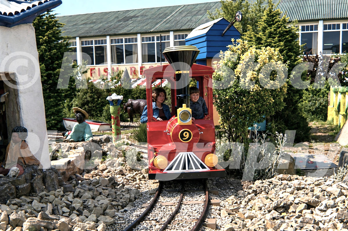 1970s Peter Pan Railway ride at Butlins Bognor Regis with children in a bright red miniature locomotive running through a landscaped miniature scene