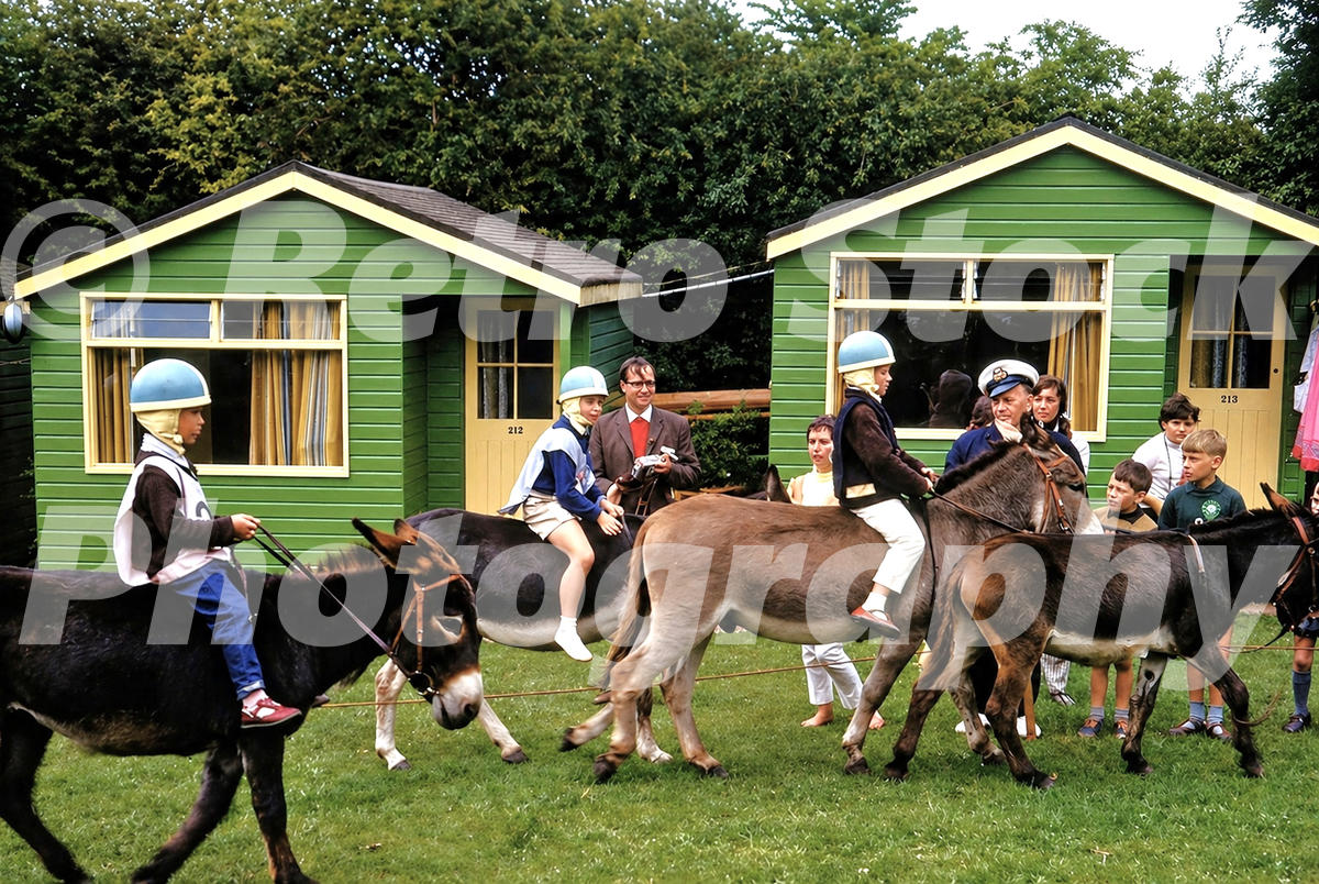 Pontins South Devon Holiday Camp donkey derby at Paignton in the 1960s with child riders, spectators and green timber chalets