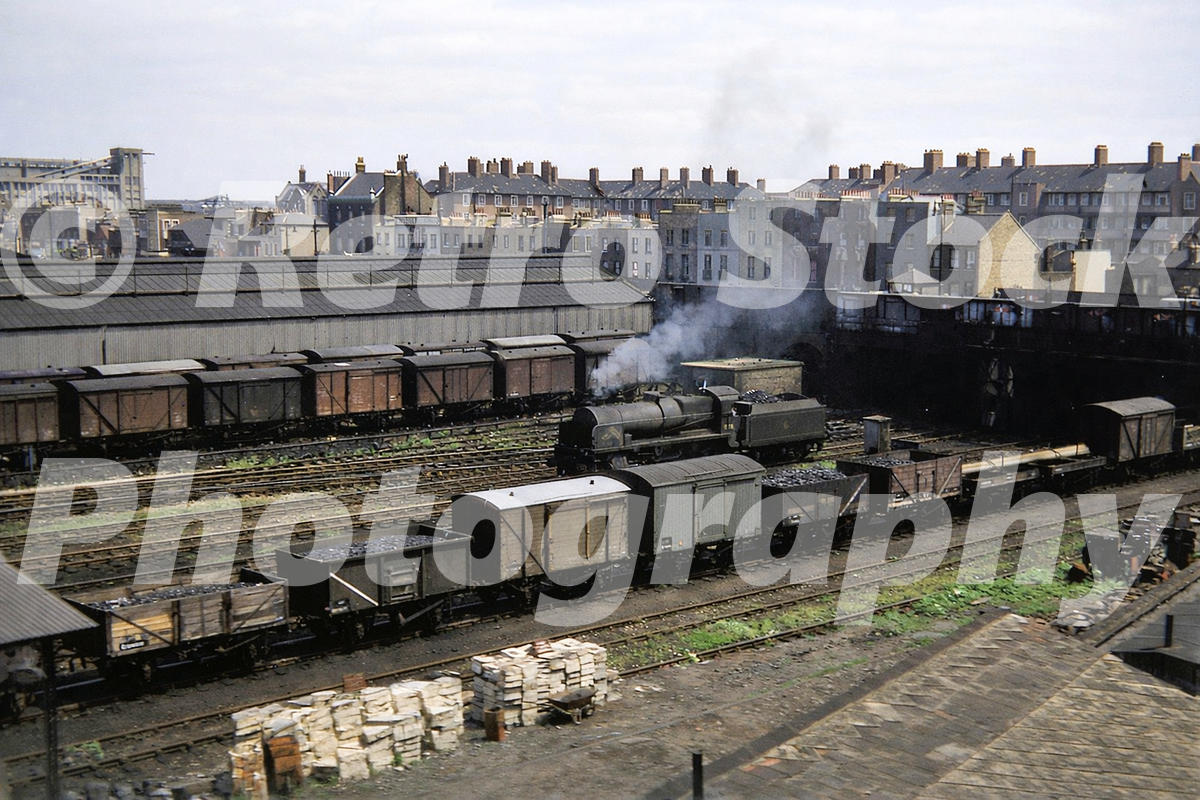 Vintage 1950s colour photo of a railway yard south of the Thames near Battersea Park Road in London, with goods wagons, a steam locomotive and the Savona Street Estate behind.