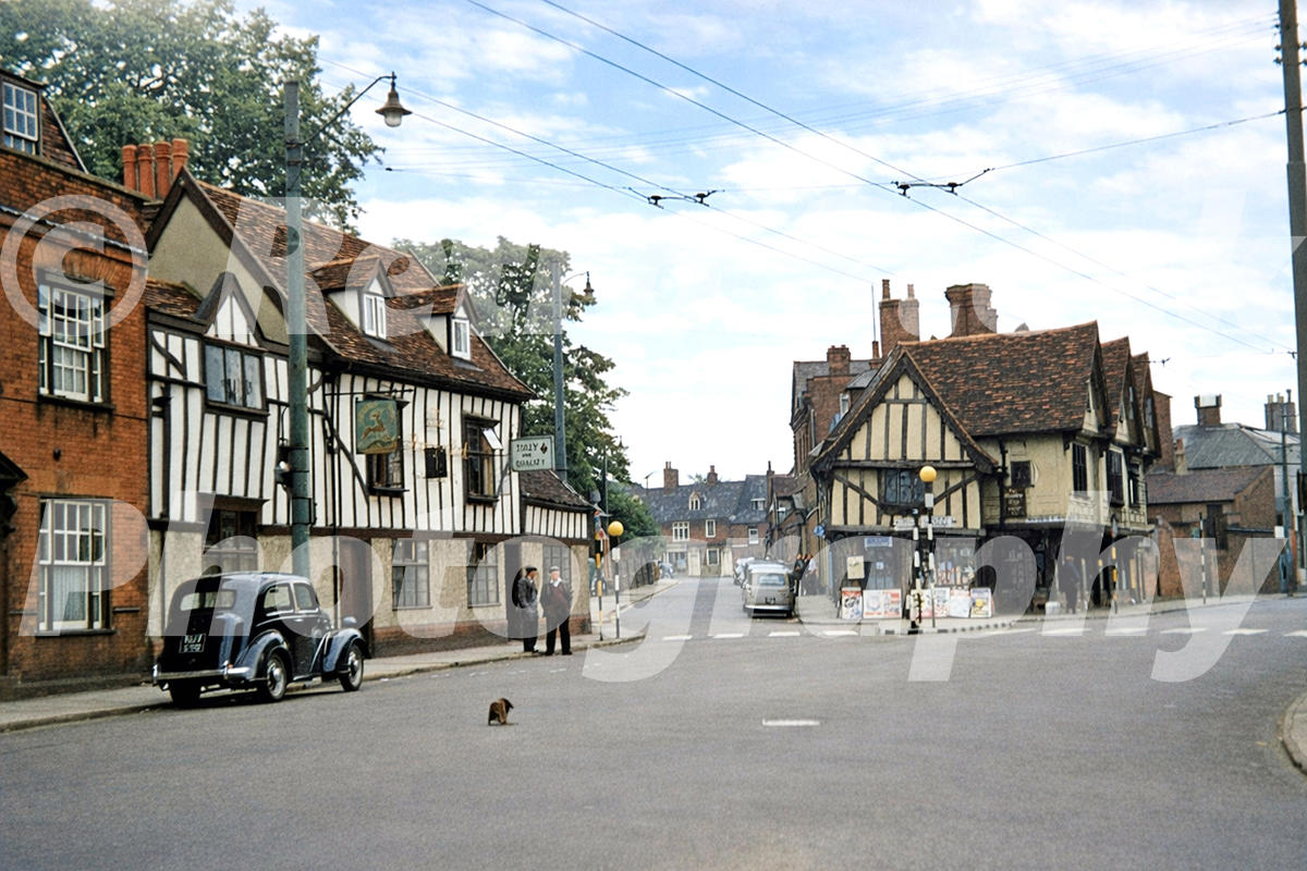 1950s view of St Margaret’s Street in Ipswich, with timber-framed buildings, the Halberd Inn, trolleybus wires, cars and traffic bollards.