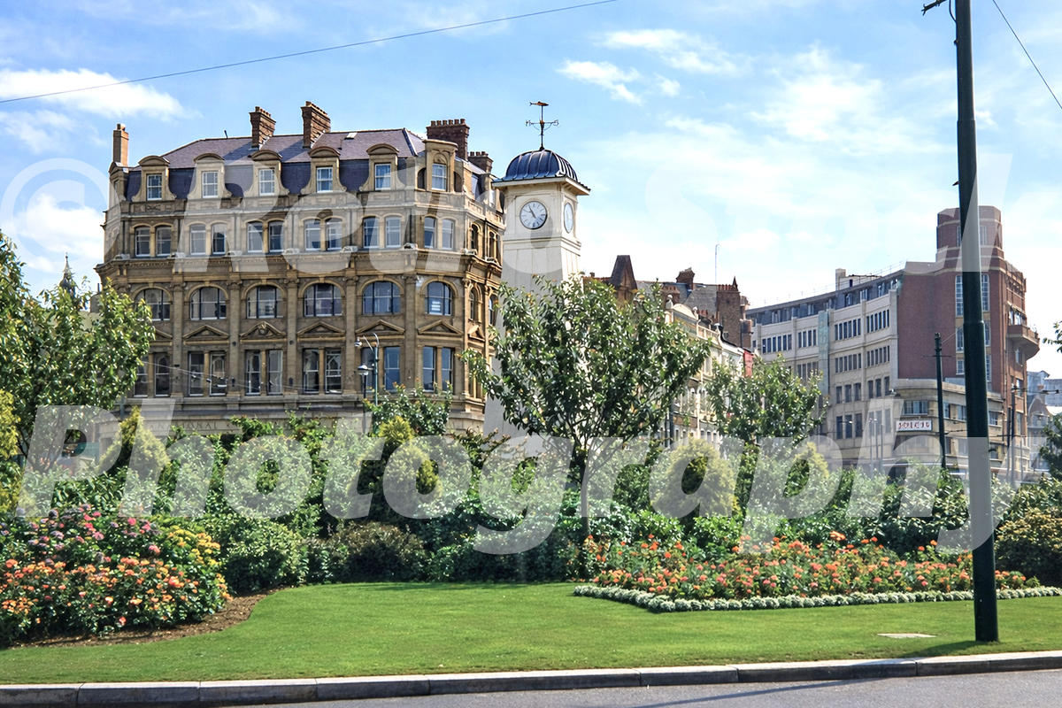 1950s colour photo of The Square in Bournemouth, with gardens, flower beds, the clock tower and surrounding town-centre buildings.