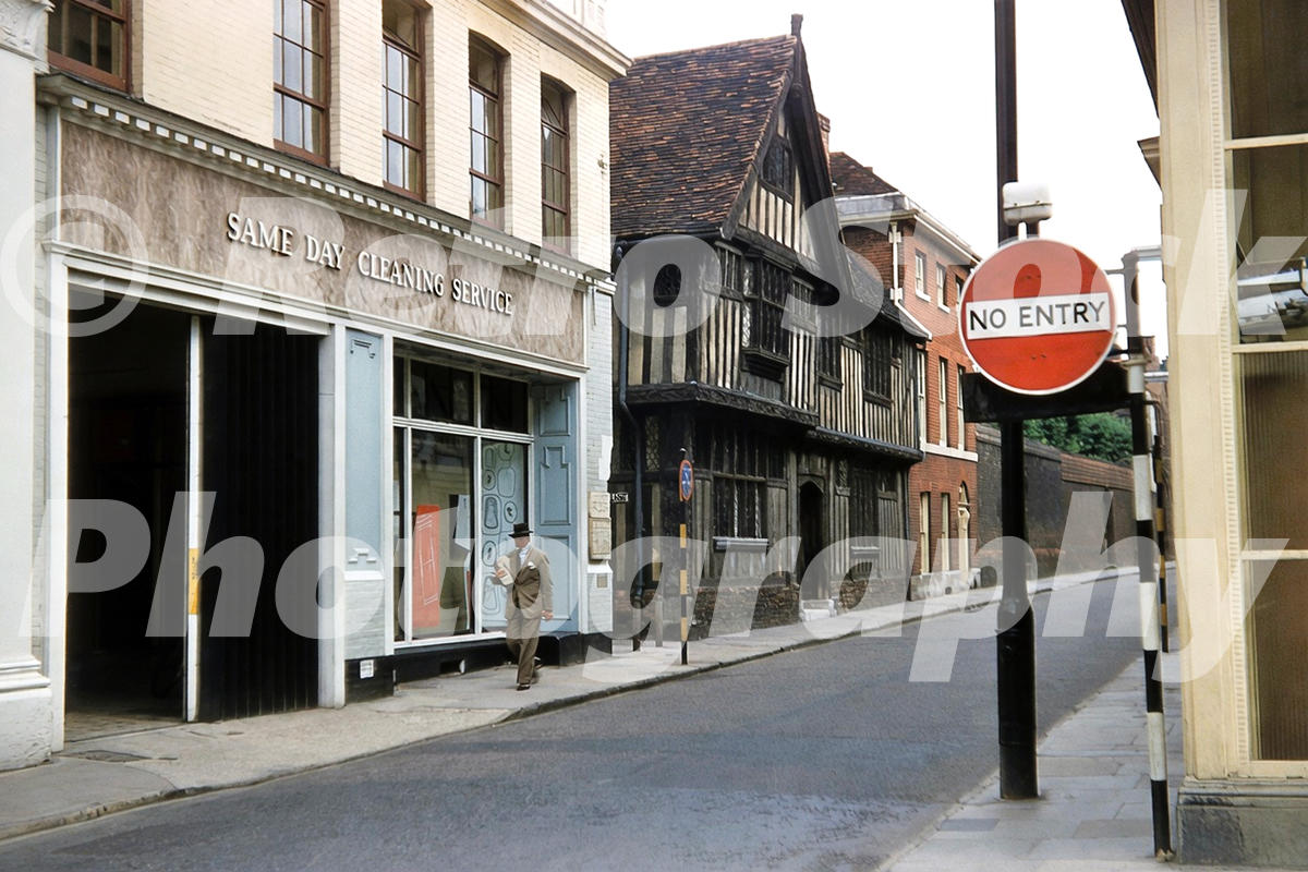 1950s colour photo of Upper Brook Street in Ipswich, with a same day cleaning shop, a No Entry sign and a timber-framed building in the background.