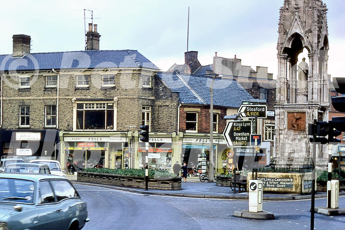 A 1970s photograph of the Clarkson Memorial in Wisbech, featuring the ornate stone monument, the Fells radio and television shop, and road signs for Sleaford and Kings Lynn.