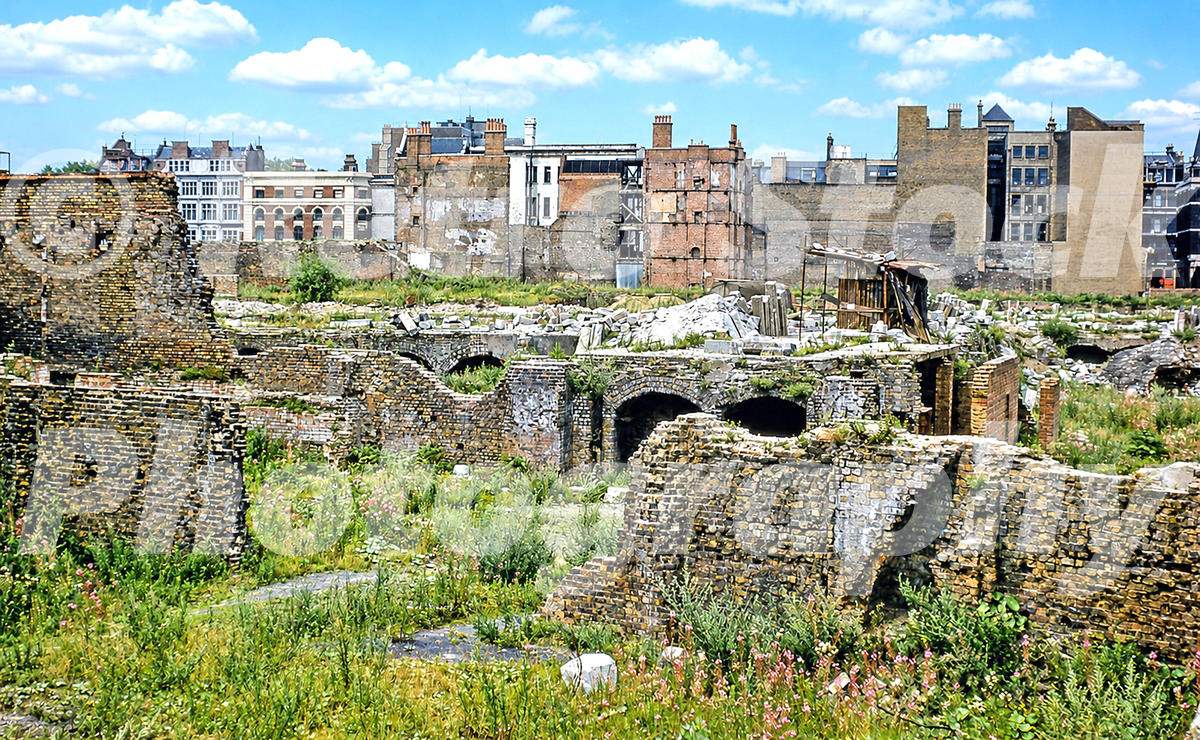 A 1950s colour photo of the extensive bomb damage and ruins in the Cripplegate area of London, featuring derelict brick foundations and wildflowers growing amongst the rubble.