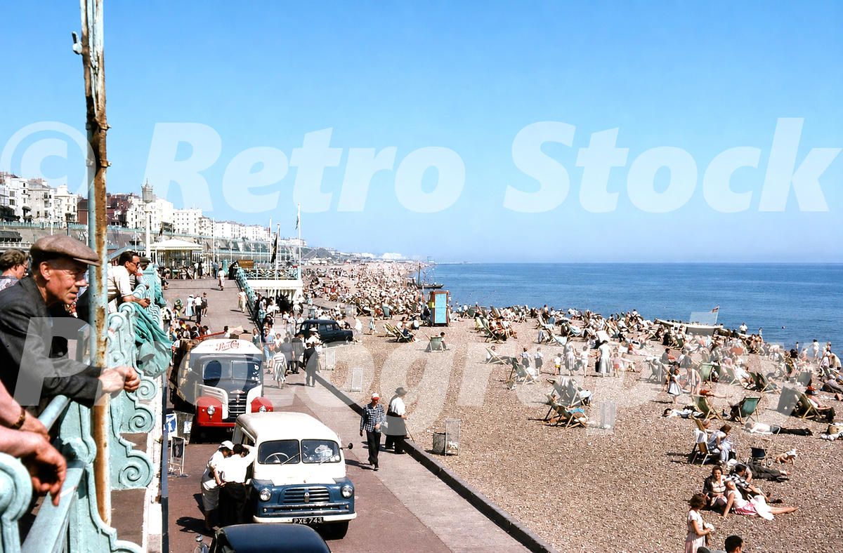 1950s photo of Brighton seafront and beach, with crowded deckchairs, promenade railings, a Pepsi-Cola drinks lorry, service vehicles and holidaymakers along the shore.
