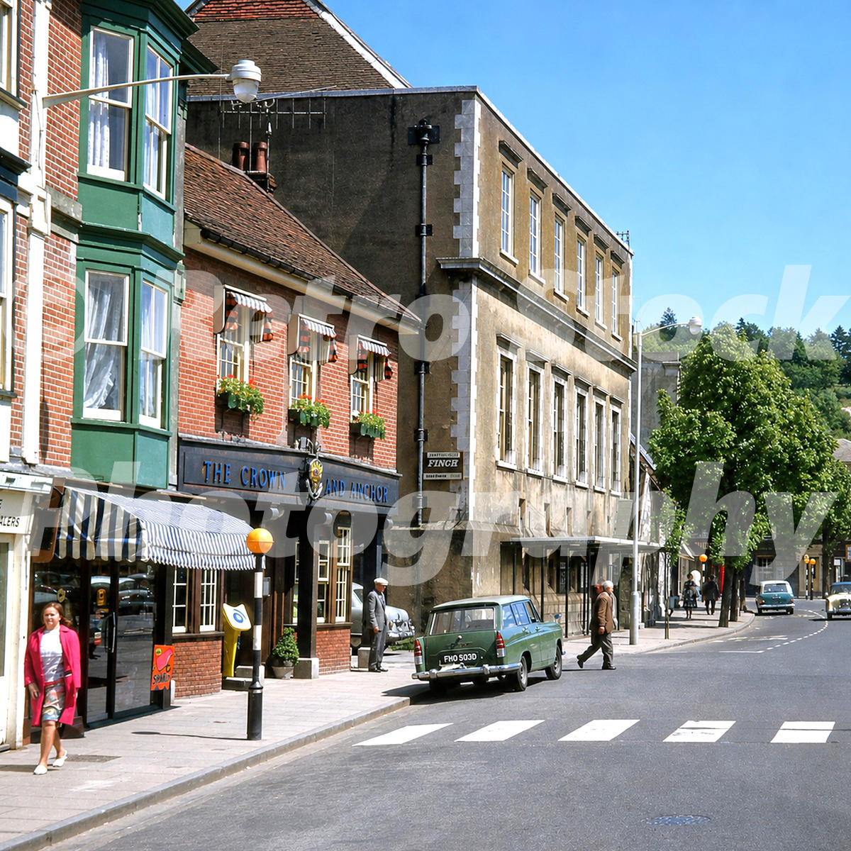 1960s view of Broadway in Winchester, Hampshire, with The Crown and Anchor pub, an Austin Cambridge estate, pedestrians and shopfronts.
