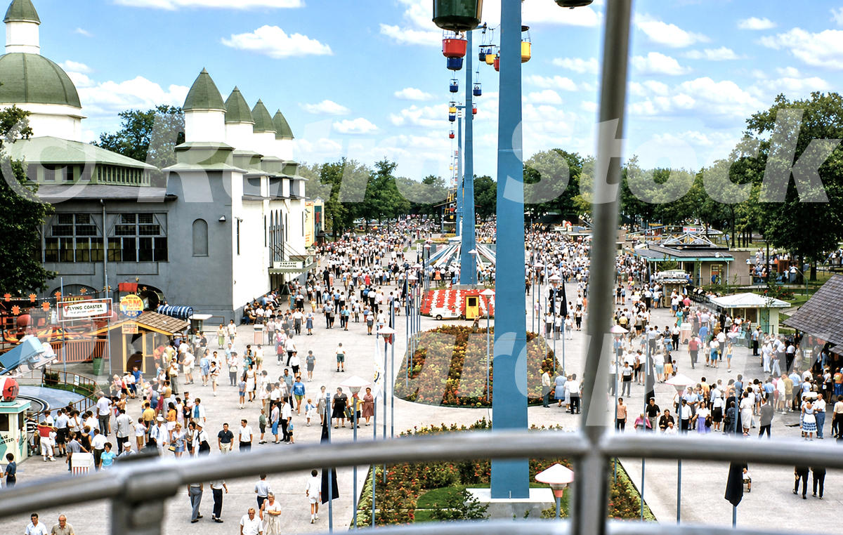 A 1960s color photo of the Cedar Point midway in Sandusky, Ohio, featuring the Sky Ride gondolas overhead, a crowded pedestrian walkway, and the Coliseum building on the left.