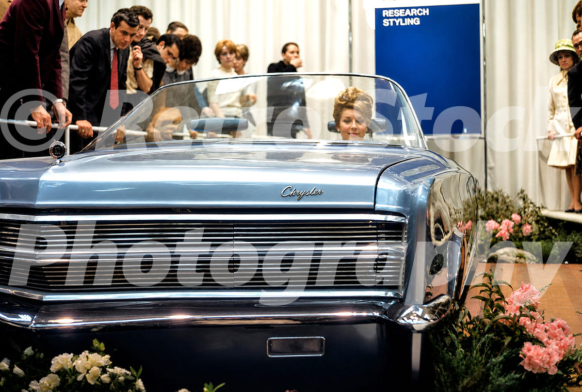 A 1960s color photo of the Chrysler 300X concept car at the 1966 New York Auto Show, featuring a joystic steering system and a model in the driver's seat.
