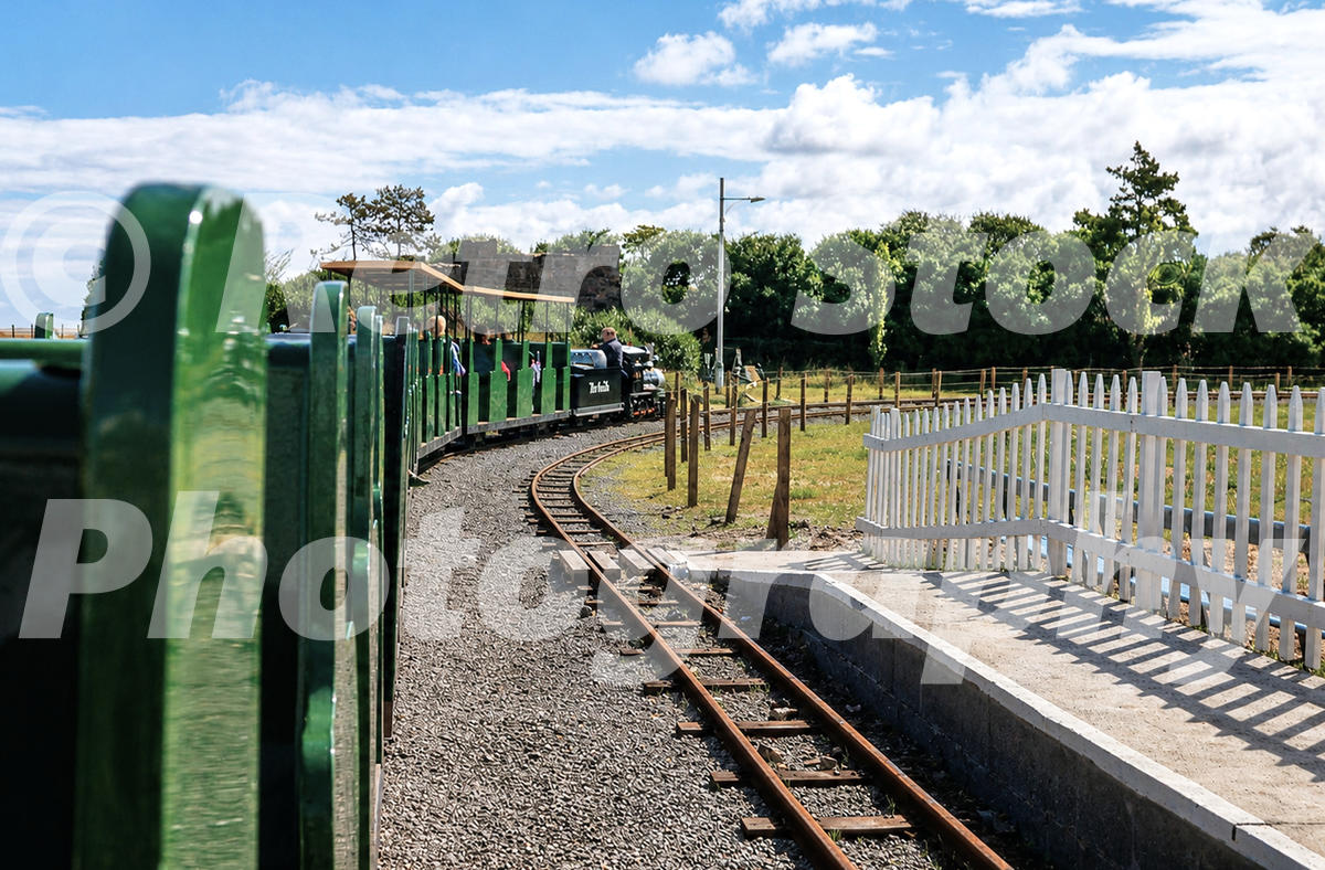 1970s view from a train on Cleethorpes Miniature Railway, with track, green carriages, white fencing and a small platform.