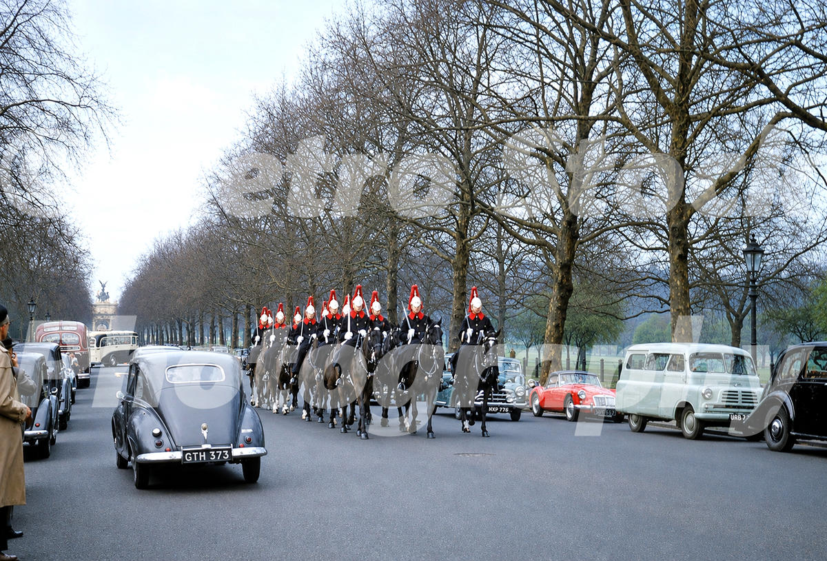 A 1950s colour photo of the Queen’s Guard of the Royal Horse Guards riding down Constitution Hill in London, with a grey Jowett Javelin and other vintage cars in the foreground.