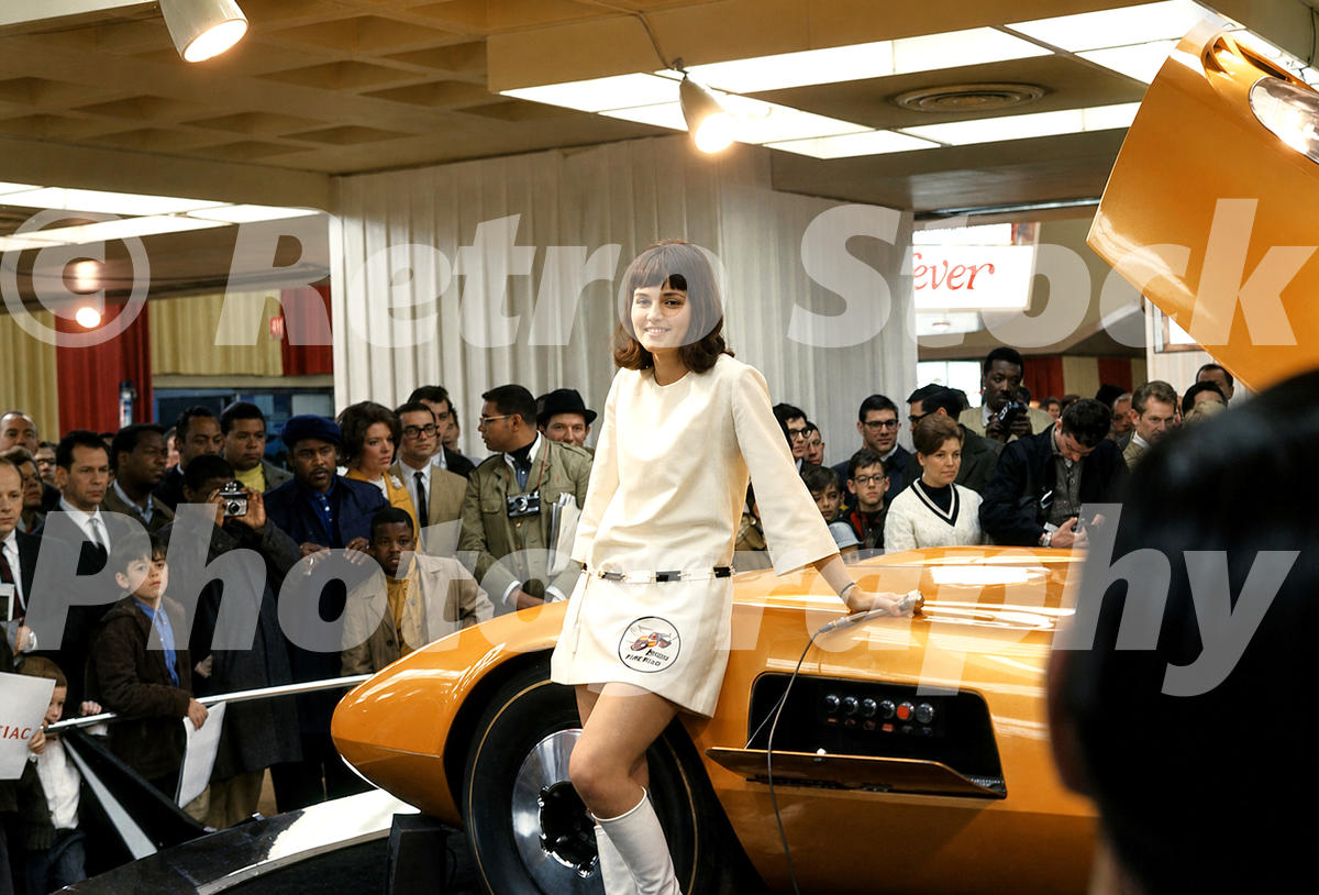 A 1960s color photo of a model in a white mod-style dress leaning against the orange Dodge Charger III concept car at the 1968 New York Auto Show.