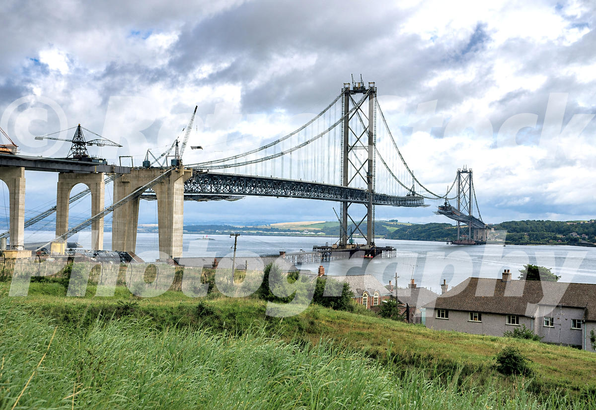 Vintage 1960s photo of the Forth Road Bridge under construction above the Firth of Forth, with cranes, incomplete deck sections and suspension towers.