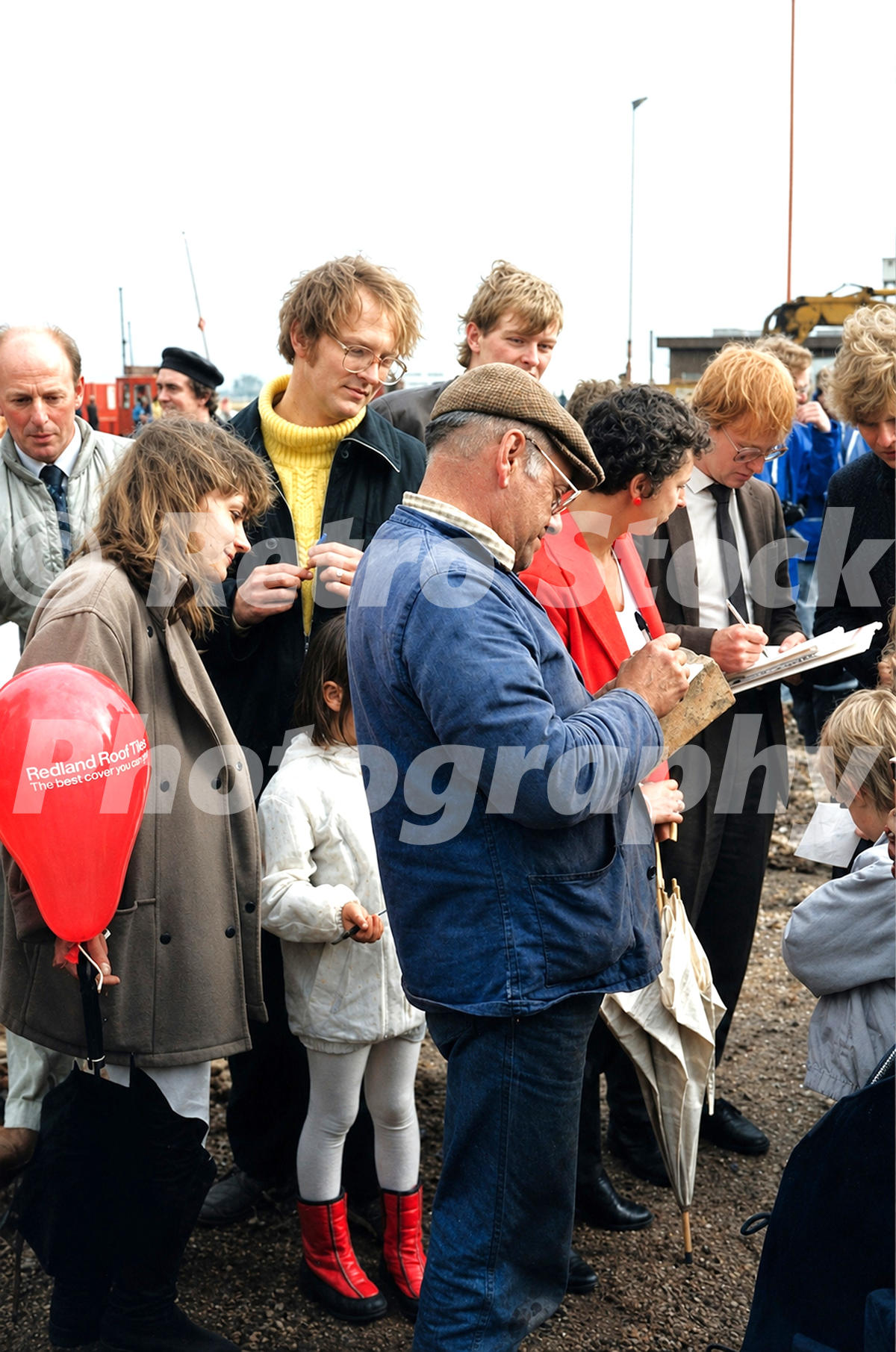 1980s view of Fred Dibnah signing bricks after demolishing a chimney at the Redland Roof Tile factory in Leighton Buzzard, with a crowd gathered around.