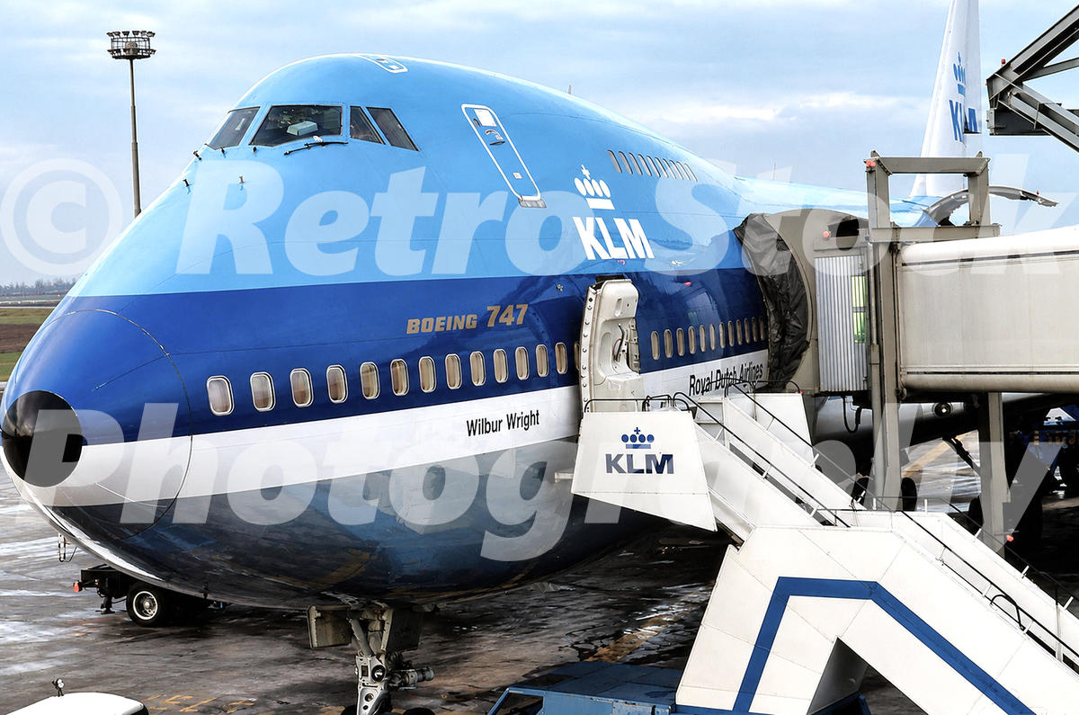1970s view of KLM Boeing 747 Wilbur Wright at Schiphol Airport, Amsterdam, with boarding stairs, jet bridge and classic blue KLM livery.