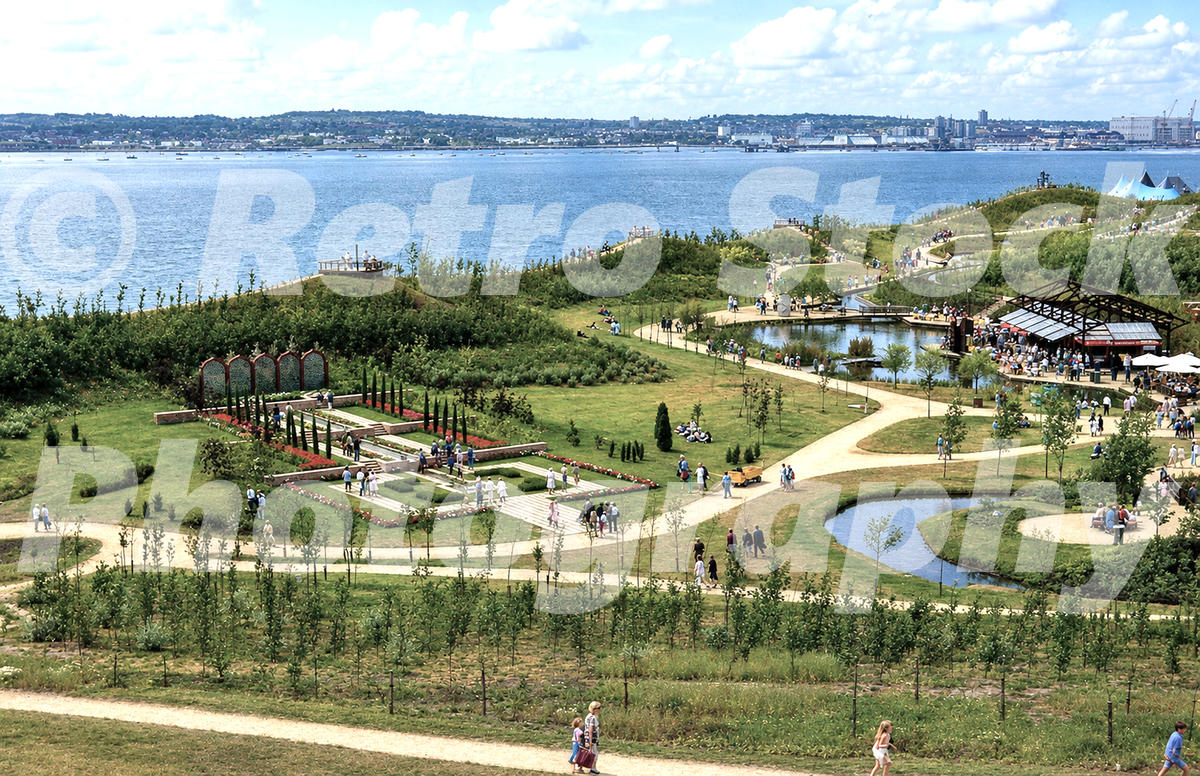 1980s view of the Liverpool Garden Festival beside the River Mersey, with landscaped gardens, ponds, paths, visitors and the opposite shoreline beyond.