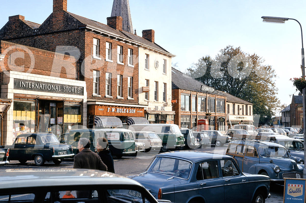 A 1970 photograph of Market Place in Long Sutton, featuring International Stores, F.W. Hole & Son butchers, and numerous period cars and vans parked in the square.