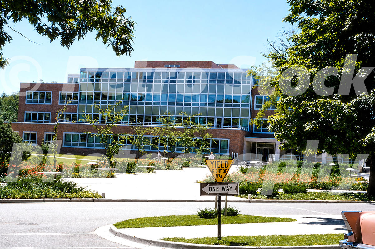 A 1950s color photo of the Student Services Building at Michigan State University in East Lansing, featuring mid-century brick and glass architecture with a Yield Right of Way sign in the foreground.