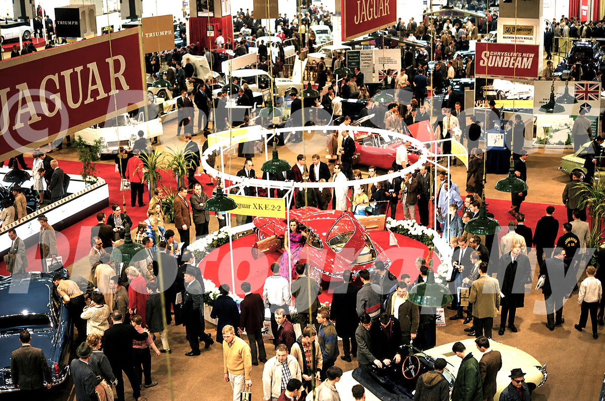 A 1960s colour photo taken from a high angle of the Jaguar exhibition stand at the 1966 New York Auto Show, featuring red and yellow E-Types and large Jaguar banners.