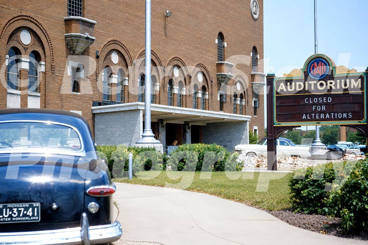 1950s color view of the original IMA building in Flint, Michigan, with auditorium sign, parked cars and entrance under alteration.