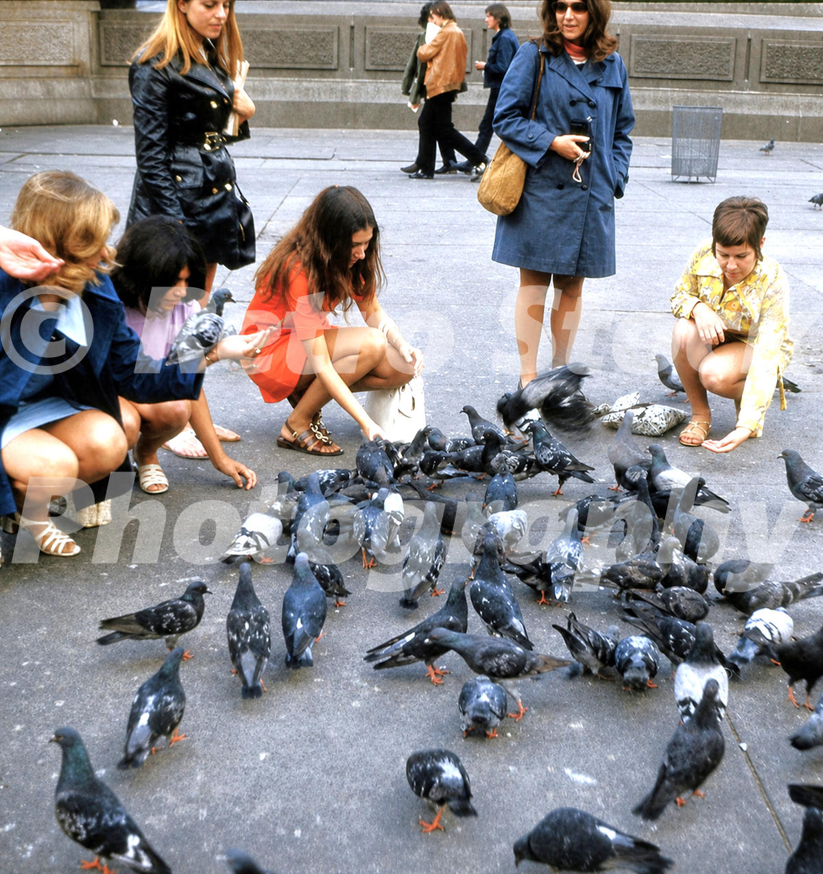 1970s photo of women feeding pigeons in Trafalgar Square in London wearing mini skirts, boots and coats