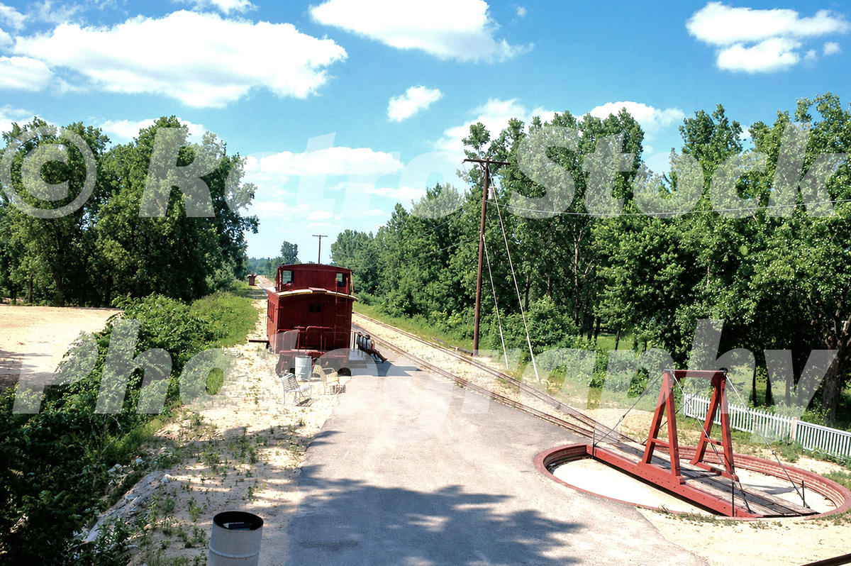 1960s color view of the Quinsippi Central Railway terminus on Quinsippi Island in Quincy, Illinois, with track, turntable, red station car and trees.