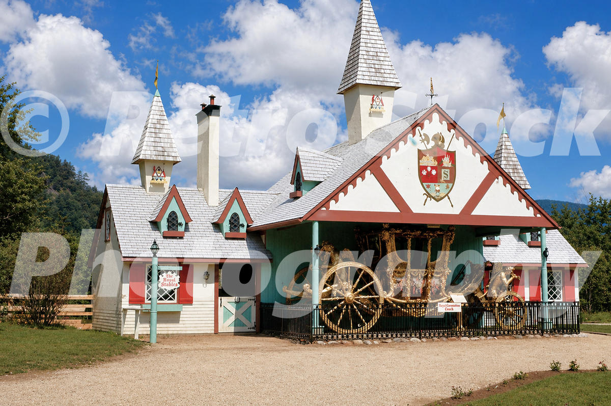 1950s color view of the Royal Stables and Coronation Coach at Story Land in Glen, New Hampshire, with fairy-tale buildings and wooded hills behind.