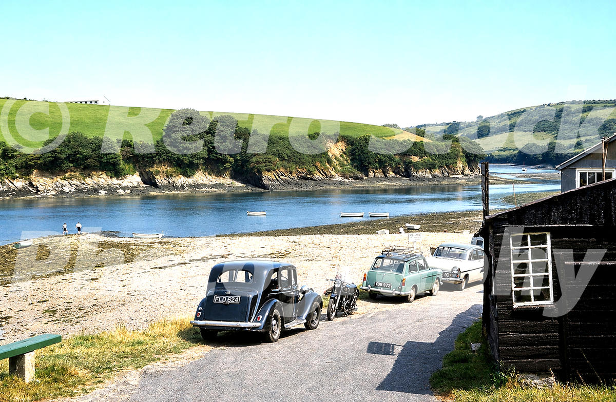 1960s view of Saint Just-in-Roseland in Cornwall, with parked cars including a blue Austin A40 Farina, a motorcycle, boats and a tidal creek.