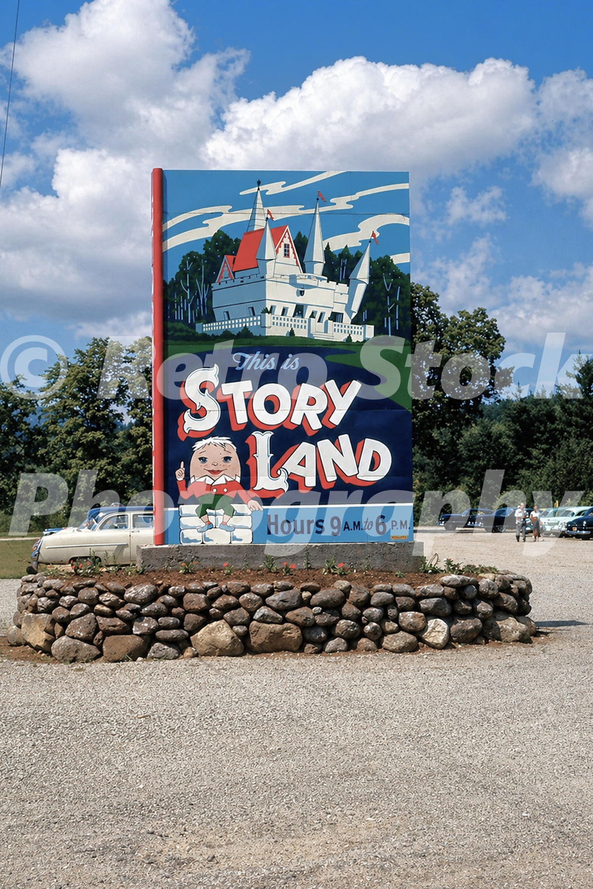 1950s color view of the Story Land entrance sign in Glen, New Hampshire, with a castle illustration, Humpty Dumpty, parking area and period cars.