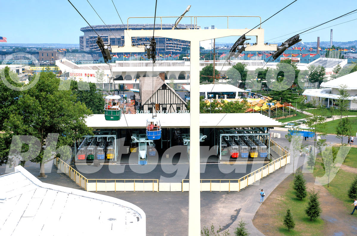 1960s color view of the Swiss Sky Ride at the New York World’s Fair, with gondola cars, the north station, Singer Bowl and Shea Stadium in the distance.