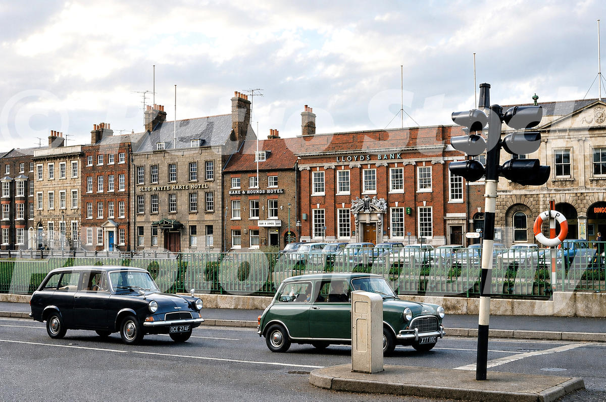 1970s view of Wisbech in Cambridgeshire, with the Olde Whyte Harte Hotel, Hare & Hounds Hotel, Lloyds Bank, traffic lights and period cars by the River Nene.